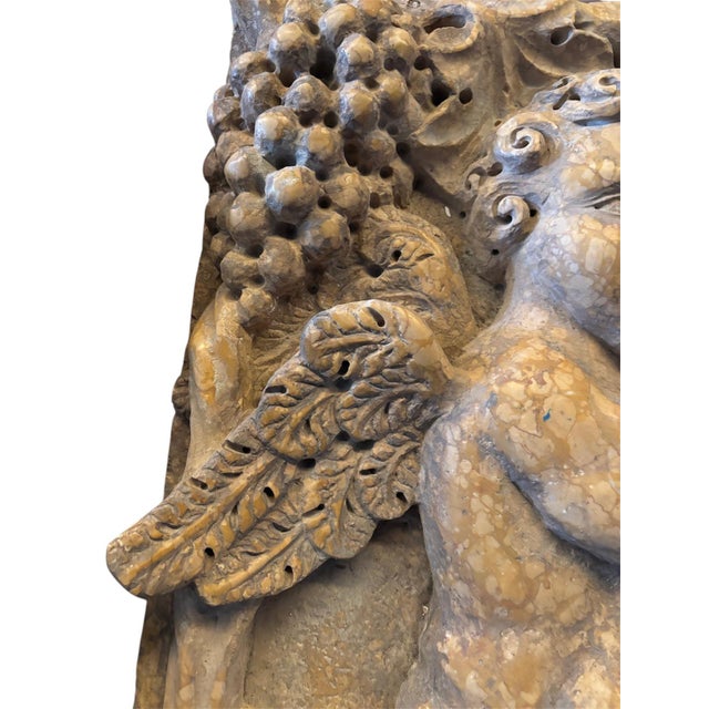 A relief in Verona Red marble depicting two winged cherubs harvesting grapes, amidst finely carved vines and leaves. The...