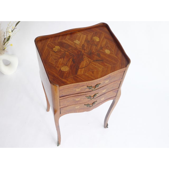A wooden French side table with beautiful inlaid floral details. The classy tall nightstand has table made out of wood...