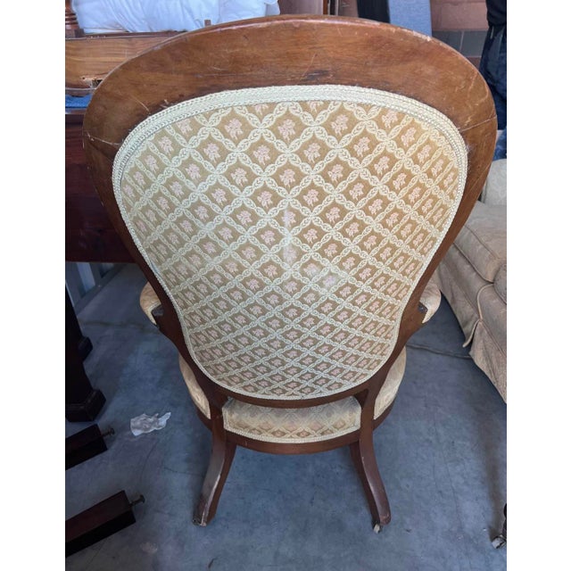 Victorian-style parlor armchair featuring a tall balloon-shaped upholstered back, carved wooden frame, padded arms, and a...