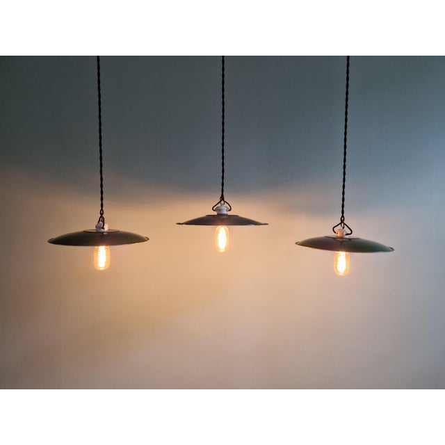 A trio of large industrial pendant lights in green enameled sheet metal with porcelain sockets, dating from the mid-20th...