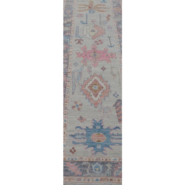 This long Oushak runner has a cream background with a light charcoal border. The border has a leaflet-like design is...