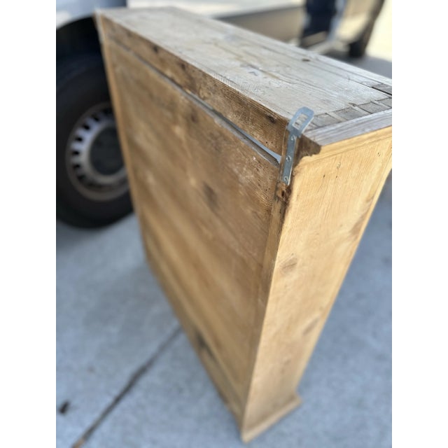 This hanging cabinet is crafted from natural wood, featuring a rustic and minimalist design. It has a rectangular frame...