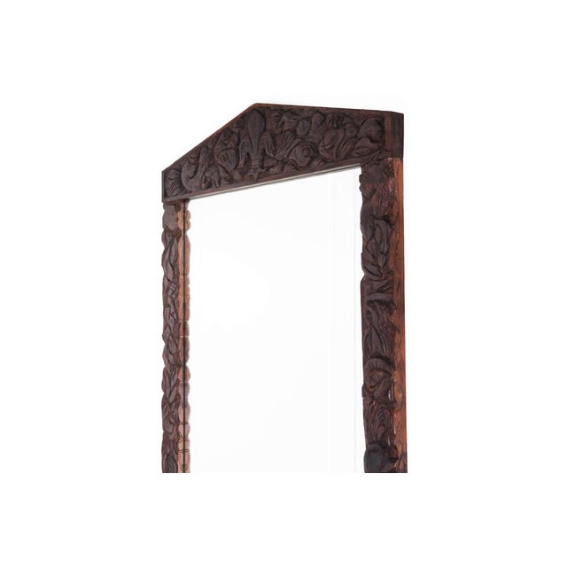 A striking large-scale mirror featuring a richly hand-carved wooden frame adorned with flowing organic motifs. The frame...
