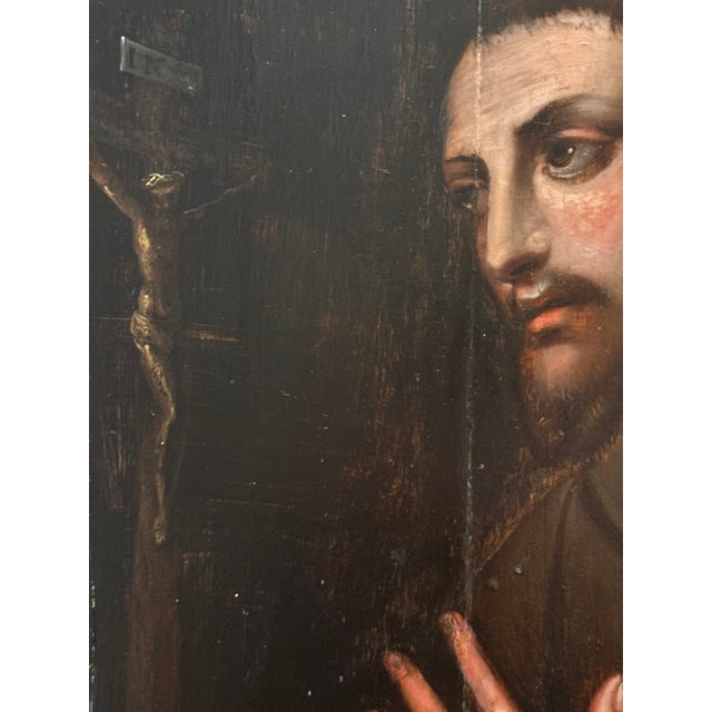 This painting depicts a Franciscan saint, most likely Saint Francis of Assisi, shown in bust form, his arms crossed over...