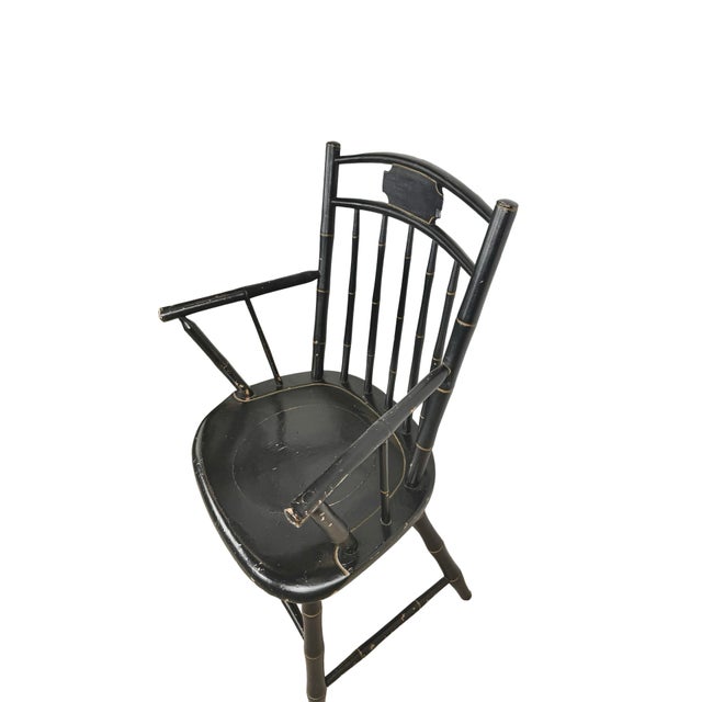 A vintage Windsor-style armchair with a black painted finish and fine gold-toned detailing. The open spindle back rises to...