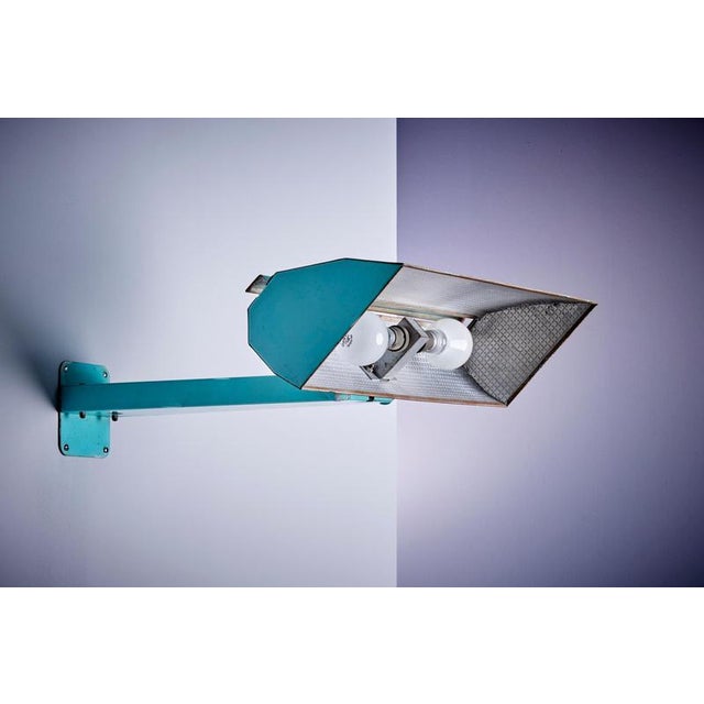 This mid-century French wall lamp features a turquoise metal frame and a geometric shade with dual bulbs behind a textured...