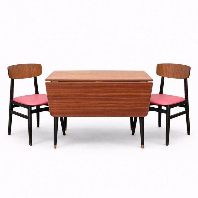 A stylish mid-century teak drop-leaf dining table with distinctive atomic-style tapered legs and brass feet, accompanied...