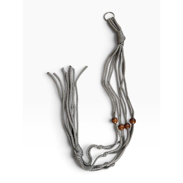 Vintage gray/taupe macramé plant hanger featuring traditional knotted construction, natural wood beads, a hanging ring,...