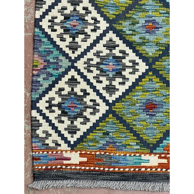 Afghan Kilim rug, hand-knotted in Afghanistan from 100% wool. Measuring 9’10” x 15’5”, the rug features an all-over...