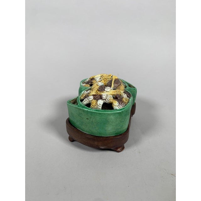 CHINA, 18TH CENTURY, KANGXI PERIOD (1661-1722) Biscuit porcelain and Sancai enamel incense burner resting on a carved...