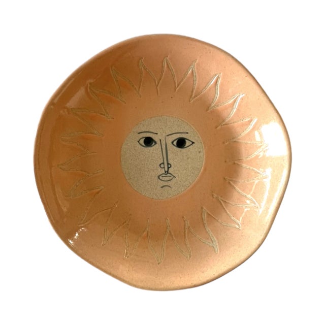 A handmade stoneware plate with a natural tan base with a peach-colored glaze and a sun illustration 7.8"