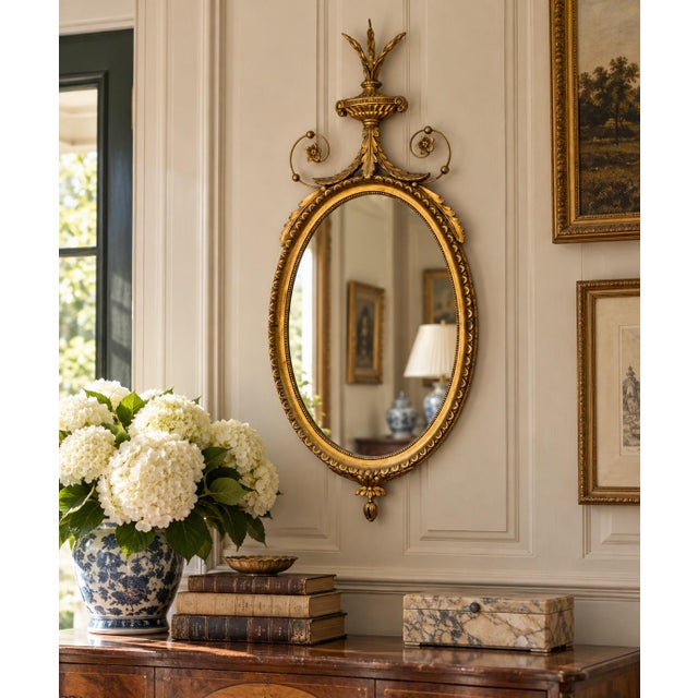 An elegant early 20th-century oval wall mirror in the Neoclassical Adam tradition, with a finely proportioned giltwood and...