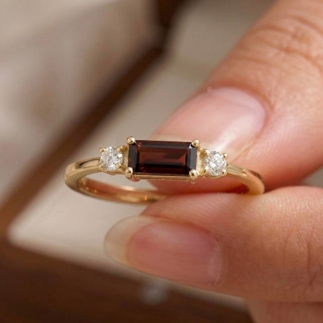 Capture effortless elegance with this minimalist, east-west baguette ring. Featuring a rich, deep-red natural garnet...