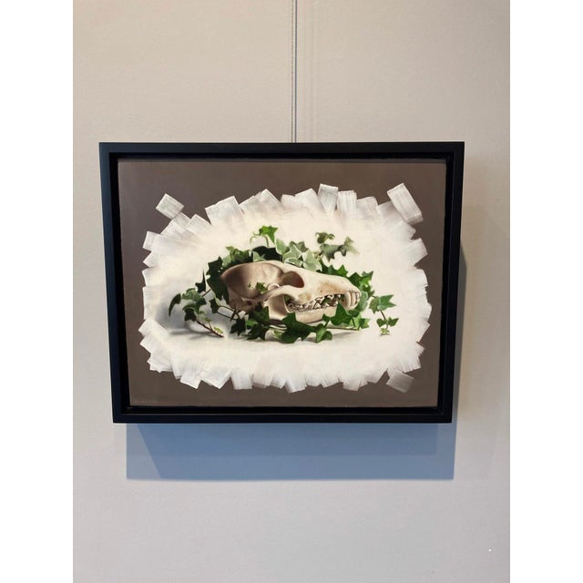 This oil on panel painting features a detailed animal skull entwined with vibrant green ivy, creating a striking contrast...