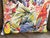 A scarlet macaw perches on the right. A toucan faces left from the lower corner. A yellow parrot pushes through tropical...
