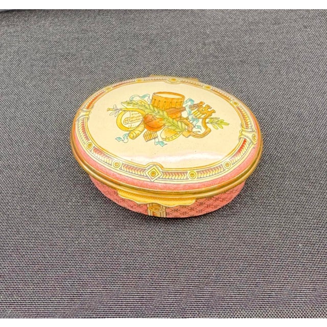 Vintage elegant oval jewelry box, featuring a pink and gold design. The lid opens to reveal a smooth, cream-colored...