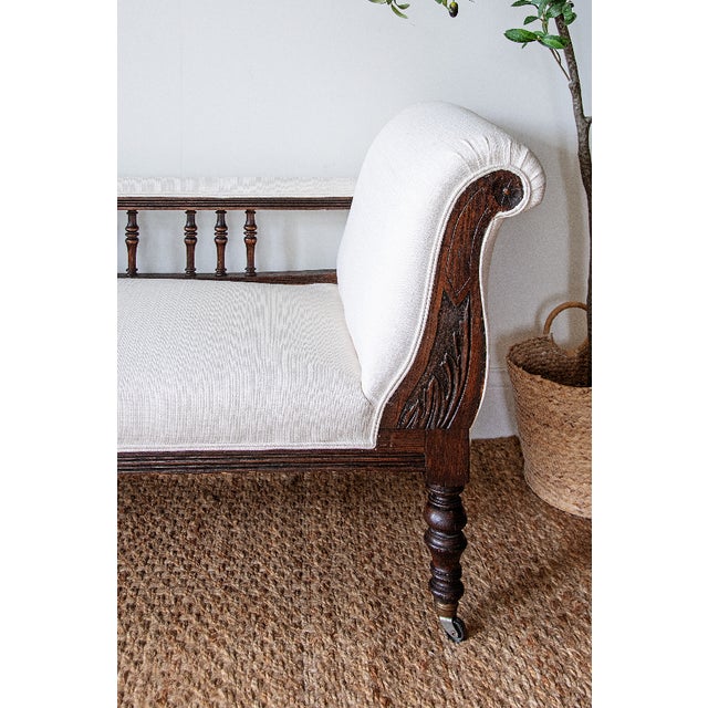 A graceful chaise longue in carved oak with a single scrolled back, dating to the late nineteenth or early twentieth...