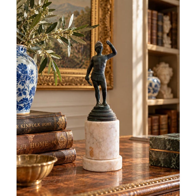A Grand Tour–style classical figure in brass, mounted on a cylindrical marble base. The slightly more relaxed posture and...
