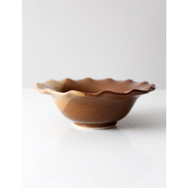 This vintage handcrafted ceramic bowl, signed by the artist, features a two-tone brown and tan glaze and a ruffled edge. A...