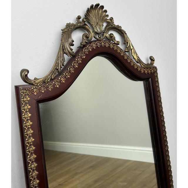 A striking vintage French mirror featuring an elegant oak frame with ornate brass decorative crest detailing to the top....