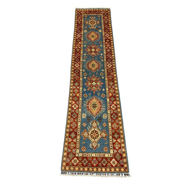 This Kazak-style wool runner has a slate blue field with repeating tribal motifs and a richly patterned rust red border....