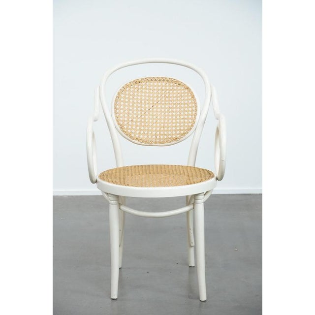 Offered for sale is this vintage white bistro chair with armrests in Thonet style, featuring an elegantly curved wooden...