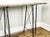 A rectangular industrial style console table with a weathered, planked wooden top, ornate wrought iron base of slender,...