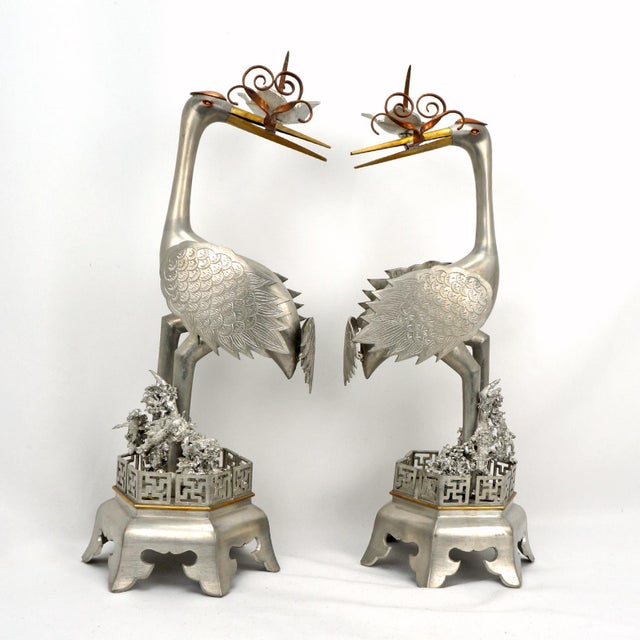 A striking pair of vintage pewter candlesticks modeled as cranes, symbolizing longevity, perched amidst dense, stylized...