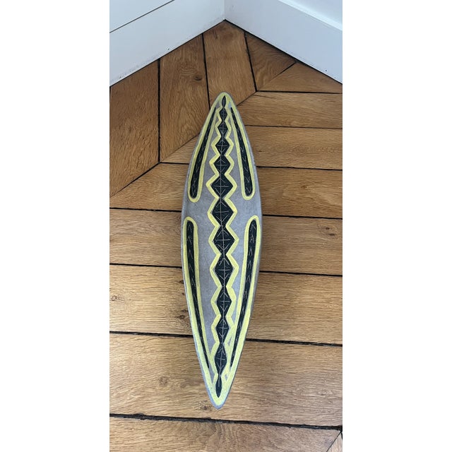 A ceramic canoe or shuttle-shaped bowl with a stylized geometric design in black and yellow on a gray background, signed...