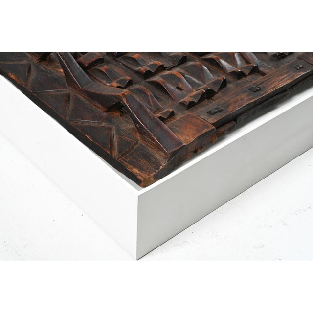 An antique carved wooden heavily patinated granary door by the Dogon people of Mali, framed in a wall mounted white...