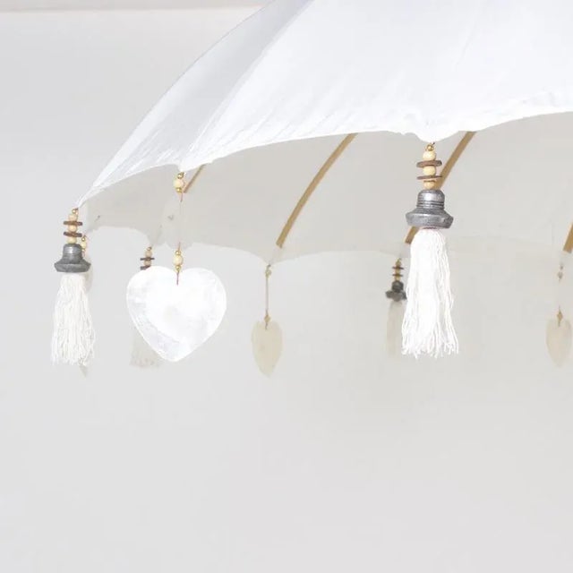 Exotic white cotton umbrella with bamboo ribs trimmed with carved wood and mother of pearl drops. The two-piece pole is...