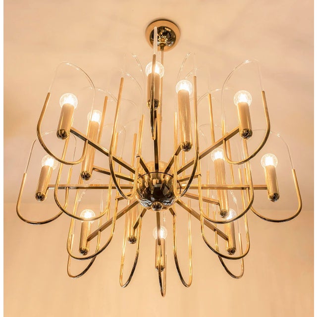 Italian mid-century polished gilt brass chandelier with clear glass elements in the holders. This chandelier includes 12...