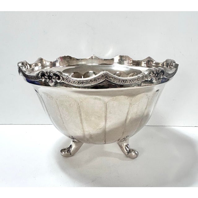 An elegant vintage silverplate centerpiece bowl with a scalloped floral rim and raised footed base, designed to reflect...
