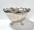 An elegant vintage silverplate centerpiece bowl with a scalloped floral rim and raised footed base, designed to reflect...