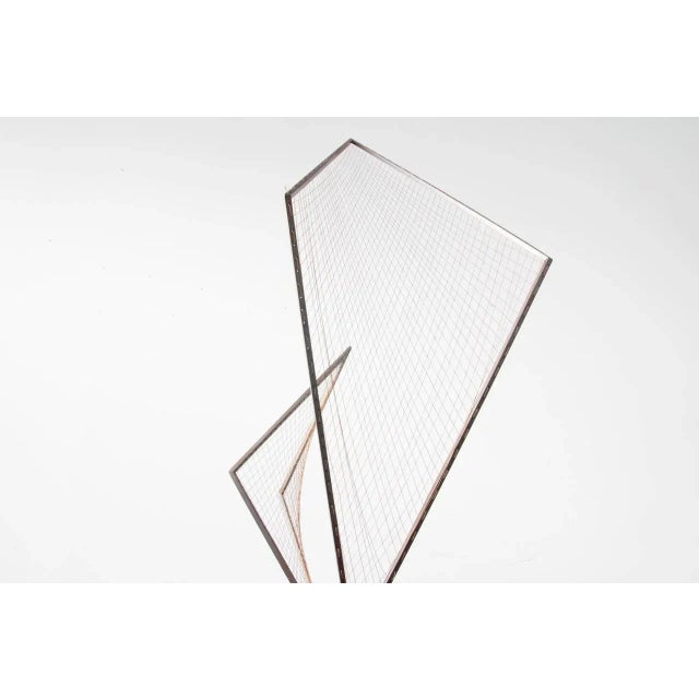 Ascending from a triangular prism base of iron, squared brass rods comprise the skeleton for a grid of strings. Fastened...