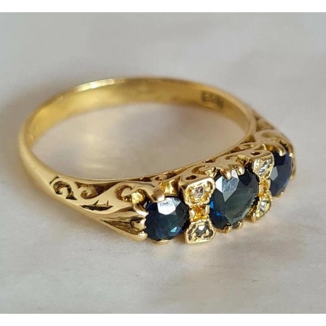 A striking vintage ring crafted in rich yellow gold and set with three deep blue faceted sapphires accented by small...
