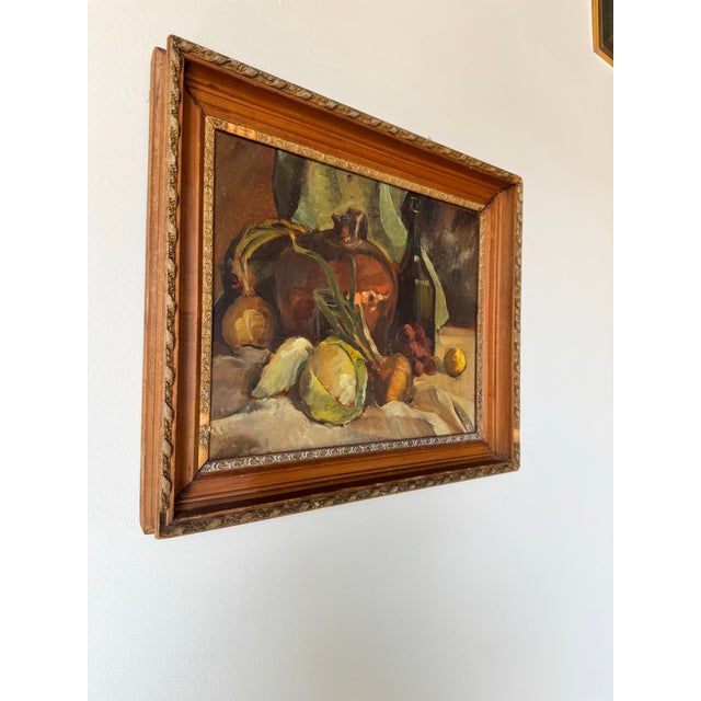 This vintage still life painting captures a beautifully arranged composition of rustic elements, including onions, a...