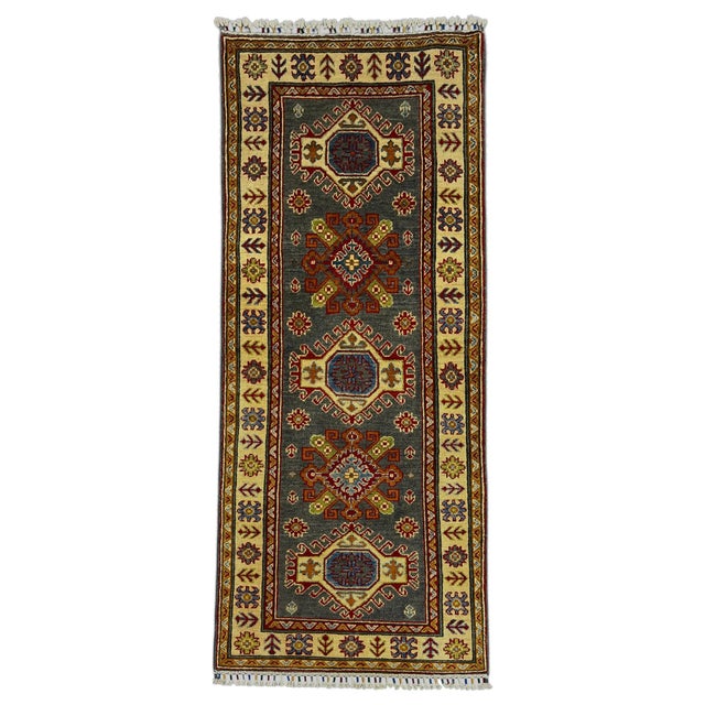 This natural dye wool runner features a charcoal gray field with repeating Kazak-style geometric motifs. A cream border...