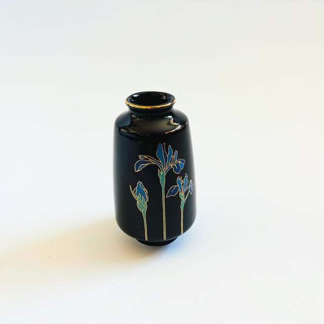 A petite glossy black vintage ceramic bud vase. Features the image of an iris with gold accents applied to the surface on...