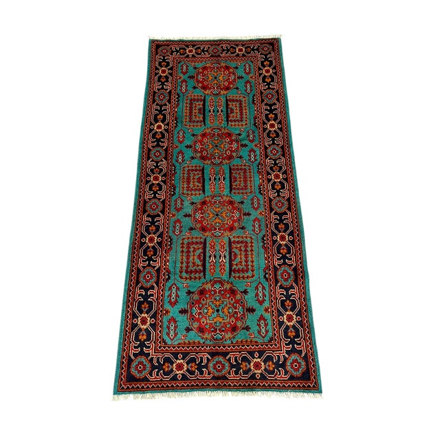 Four red floral medallions run down the turquoise field of this wool runner, surrounded by smaller geometric motifs. A...