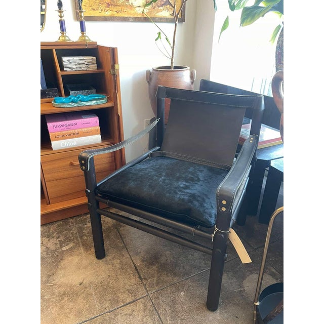 The L1888-01 armchair features a black leather sling-style back and arm panels secured with brass rivet detailing. The...