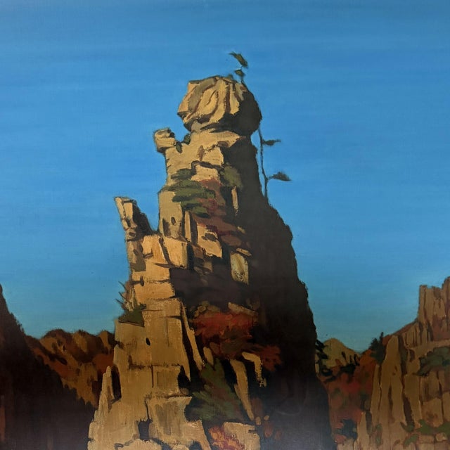 This atmospheric landscape painting depicts a dramatic mountain range with steep rock formations set against a clear blue...