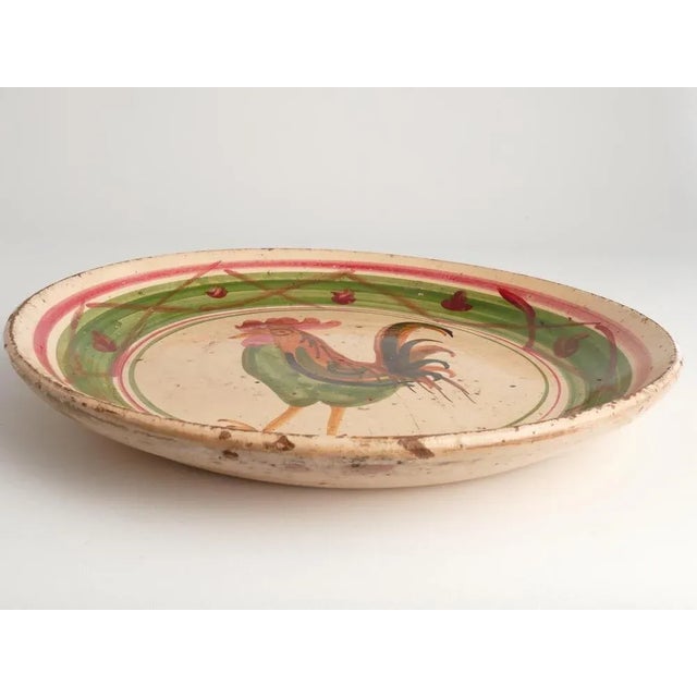 A large milk bowl crafted from ball clay features a rooster motif in red, green, and brown. This piece, originating from...