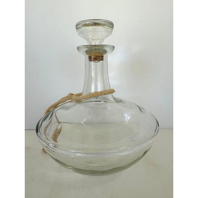 This vintage clear glass decanter features a gracefully rounded body with a narrow neck and its original fitted glass...