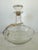 This vintage clear glass decanter features a gracefully rounded body with a narrow neck and its original fitted glass...