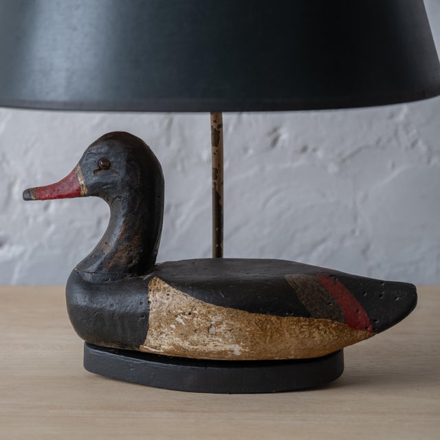 An antique duck decoy mounted as a lamp in dark green paper shade. 12 ½ inches wide by 6 inches deep by 18 ¼ inches tall;...