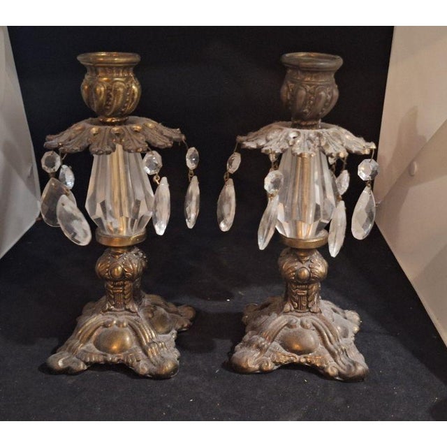 Vintage pair of brass candlestick holders with hanging crystal prisms in a Hollywood Regency style. Ornate footed base...
