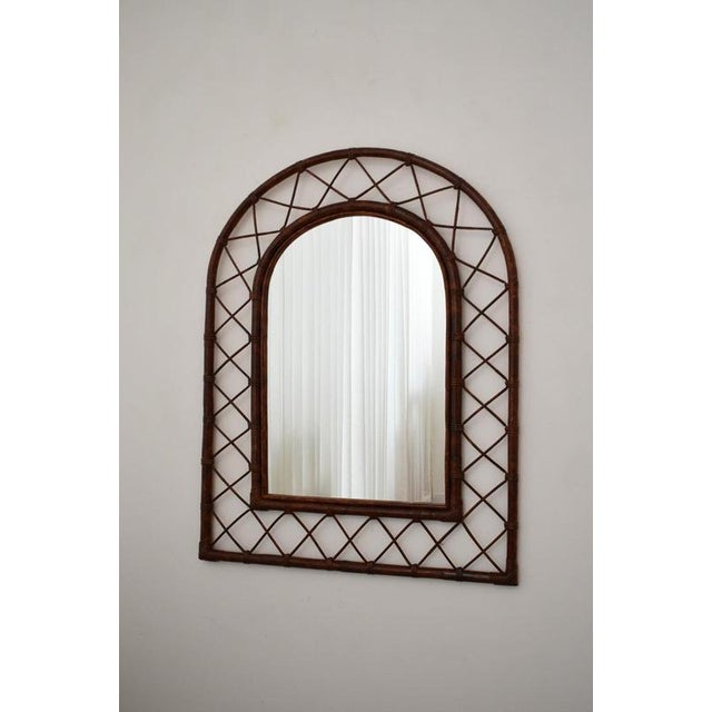 Rattan arch mirror, 1970s. Arch-top mirror with an open diamond lattice rattan frame and wrapped cane bindings, in a warm...