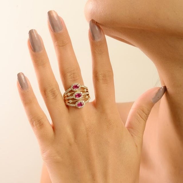 This elegant Art Deco-inspired cocktail ring is crafted in solid 14K yellow gold, showcasing three oval-cut rubies with a...