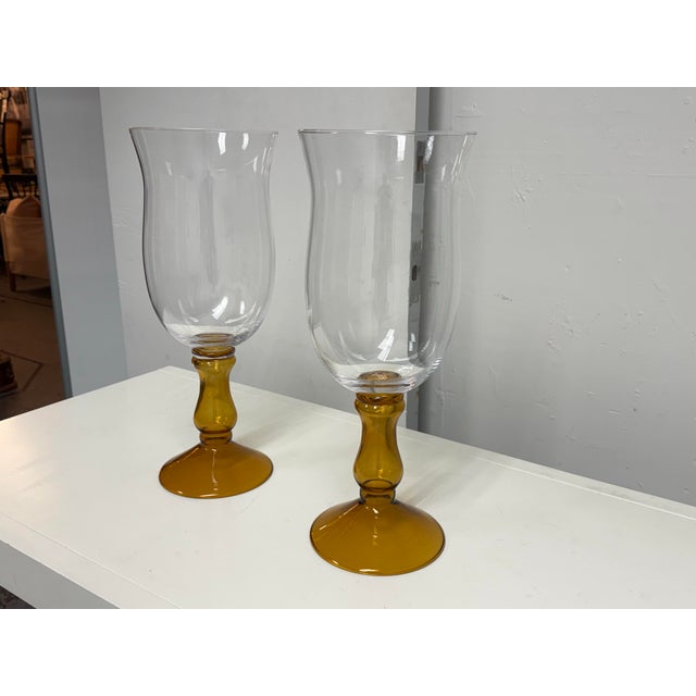 Design Plus Gallery presents a Pair of Glass Pedestal Hurricane Candleholders. Each candleholder has a clear glass bowl...
